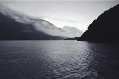 a body of water surrounded by mountains and clouds in the distance with one boat on it's side