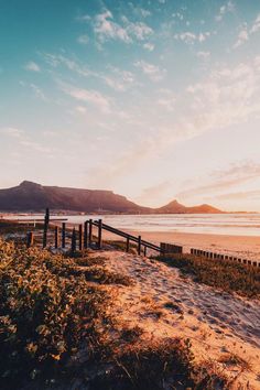 the sun is setting at the beach with mountains in the background