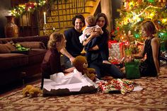 a family sitting on the floor in front of a christmas tree with presents and gifts