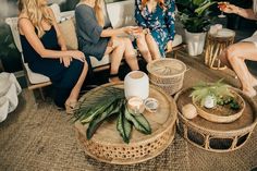 three women sitting on a couch talking to each other in a room with plants and wicker furniture