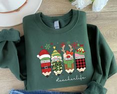 a green sweatshirt with christmas stockings and santa hats on it, next to some jeans