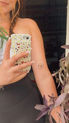 a woman holding a cell phone in her right hand and flower tattoos on her left arm