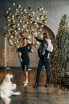 a man and woman dancing with a dog in front of a christmas tree decorated with ornaments