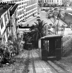 an old black and white photo of a train going down the tracks in front of buildings