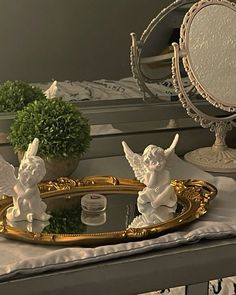 two angel figurines sitting on top of a mirror next to a potted plant