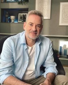 a man sitting in a chair with his legs crossed and looking at the camera while wearing a blue shirt