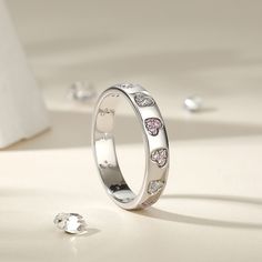 This sterling silver women's band radiates with the warmth and depth of love. Adorned with hearts of varying hues. Wrap your finger in the whimsical sparkle of this heart ring. The ring is expertly crafted from durable and shining sterling silver that features heart inlaid by multi-colored stones to add a sparkling texture to your look. It glimmers in the light, catching the eye with its simple yet striking design. The hearts are carefully set into the band, creating a harmonious and eye-catchin Adjustable White Gold Stackable Heart Ring, Adjustable Stackable White Gold Heart Ring, Silver Stackable Heart-cut Rings, Silver Stackable Rings With Sparkling Stones, Silver Stackable Heart Cut Rings, Silver Stackable Heart Ring For Wedding, Silver Round Band Jewelry For Valentine's Day, Silver Stackable Heart Ring For Promise, Silver Stackable Heart Promise Ring