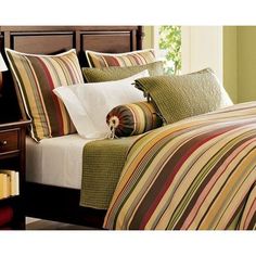 a bed with striped comforter and pillows on top of it, next to a night stand