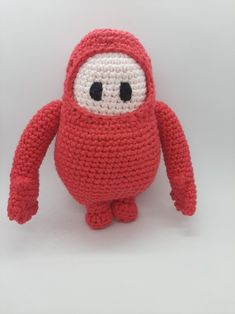 a crocheted red stuffed animal with black eyes and arms, sitting on a white surface