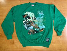 a green sweatshirt with an image of the new york jets on it sitting on a wooden floor