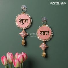 two pink and gold earrings with the word india written on them next to some tulips