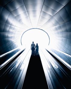 two people are standing on an escalator in a tunnel with light coming through