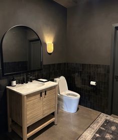 a white toilet sitting next to a sink in a bathroom under a large round mirror