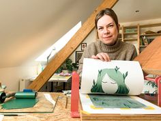 a woman sitting at a table holding up a piece of paper with an image of a horse on it