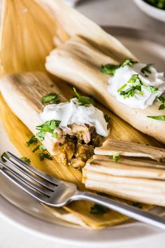 two tamales on a plate with sour cream and cilantro garnish