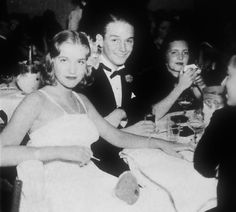 an old black and white photo of people at a dinner table with wine glasses in their hands