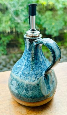 a blue and white pitcher sitting on top of a wooden table with trees in the background