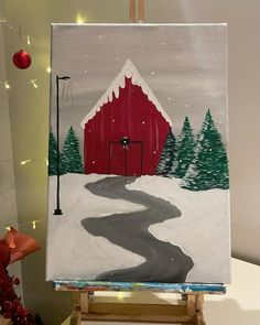 an easel with a painting on it and a red barn in the background next to a christmas tree