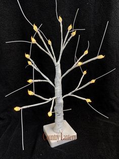 a small white tree with yellow leaves on it's branches and lights around the base