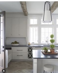 a kitchen with white cabinets and an island in front of two windows that have potted plants on it