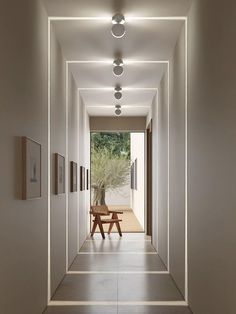 an empty hallway with two benches and paintings on the wall, leading to a dining area