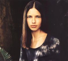 a woman with long hair standing in front of a tree and looking at the camera