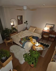 a bedroom with a bed, desk and plants in it's corner area on the floor