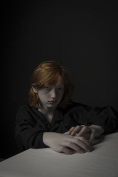 a woman with red hair sitting on top of a bed in the dark, holding her hands together