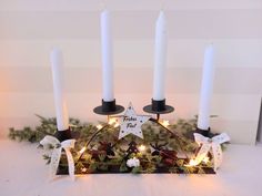 three white candles are sitting on top of a tray with pine cones and greenery