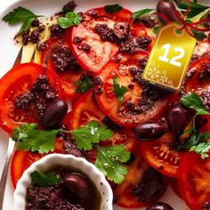 a white plate topped with sliced tomatoes and olives