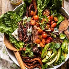 a salad with steak, tomatoes, lettuce and cucumbers in a white bowl