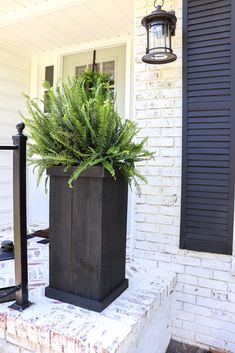 a tall planter sitting on top of a brick step next to a white house