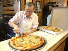 an older man cutting up a pizza on top of a counter