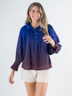 A woman smiles, wearing the Charlotte Top - Midnight Ombre with a long sleeve design in shades of blue and purple, paired with light-colored shorts. She has long hair and is standing against a plain background. Kimono Outerwear, Brand Stylist, Felt Cowboy Hats, Timeless Aesthetic, Cap Fashion, Ruffled Collar, Feminine Look, Pin Tucks, Dress And Heels