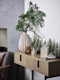 a white vase sitting on top of a wooden table next to a small house and trees