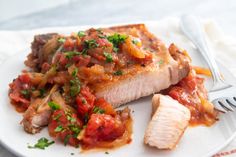 a white plate topped with fish covered in sauce and garnished with parsley