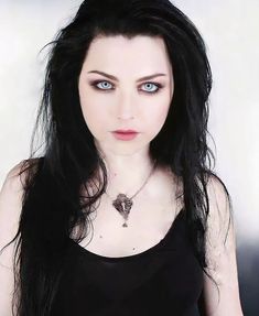 a woman with long black hair and blue eyes wearing a black tank top is looking at the camera