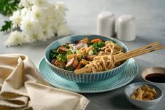 a bowl filled with noodles and vegetables next to two small bowls of dipping sauces