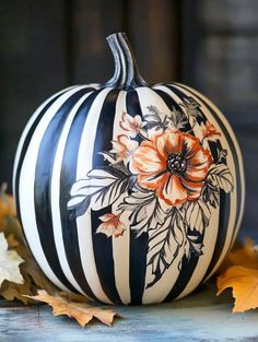 a black and white striped pumpkin with orange flowers painted on the side, sitting next to leaves