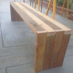 a wooden bench sitting on the side of a sidewalk next to yellow poles and chairs