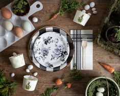 an easter table setting with eggs, carrots and other items on the wooden table