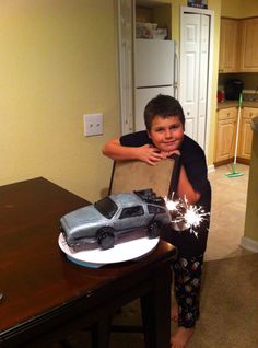 a young boy standing in front of a table with a toy car on top of it