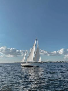 a sailboat sailing on the ocean under a blue sky with white clouds in the background