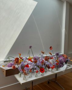 an arrangement of flowers on a table in front of a white wall