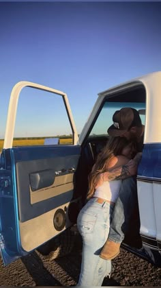 a man and woman kissing in the open door of a blue pick - up truck