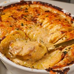 a casserole dish with chicken and cheese in it, being cut by a knife