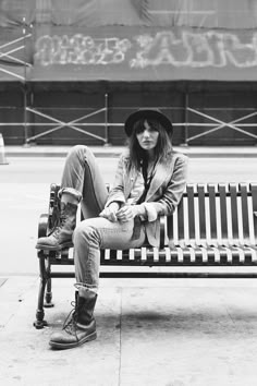 a woman sitting on top of a bench in front of a wall with graffiti written on it