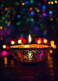 a lit candle sitting on top of a table in front of a christmas tree with colorful lights