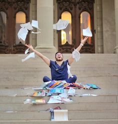 a man is sitting on the steps with his arms in the air surrounded by papers