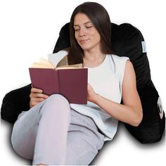 a woman sitting in a bean bag chair reading a book while holding a red book